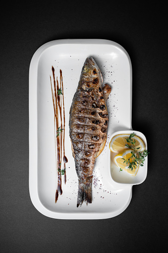 closeup of fried fish labrax with spice and lemon on plate on dark background
