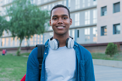 Young african american student portrait looking at camera with friendly attitude and smiling outside the campus. Photography of young adult standing alone with confidence. High quality photo