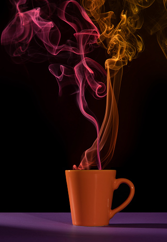 Orange cup of coffee on a purple table with red and yellow smoke against a black background
