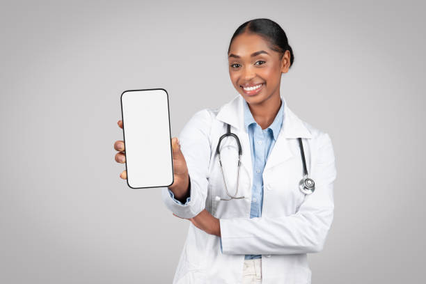 Cheerful black woman doctor in white coat hold smartphone with empty screen