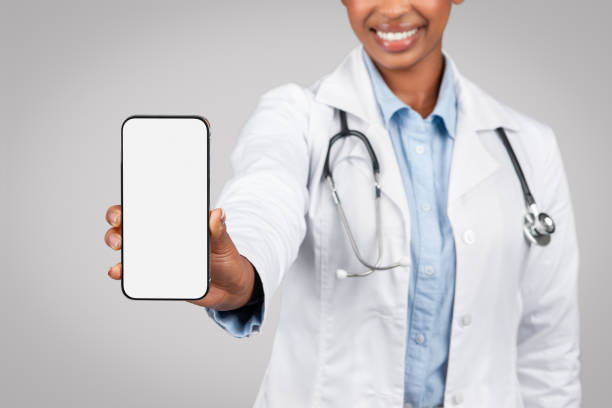 istock Glad black young lady doctor in white coat show phone with empty screen 1922984679