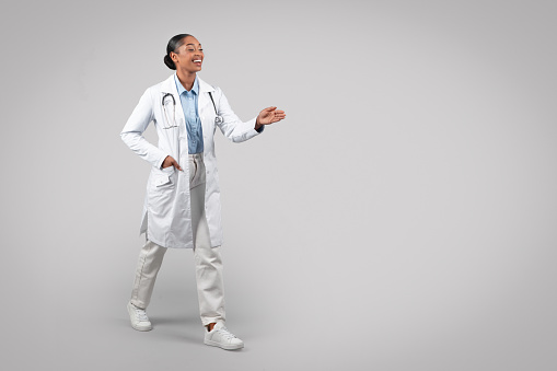 Happy friendly black millennial doctor in white coat, make handshake sign, isolated on gray studio background. Medical health care, professional exam and help, welcome, hello gesture