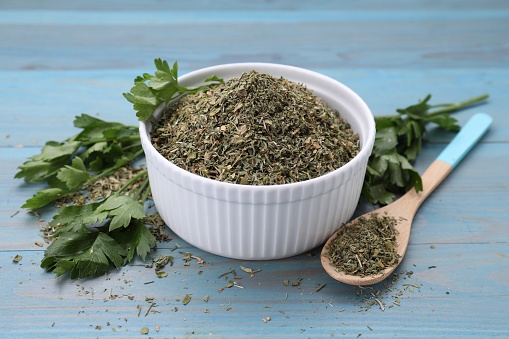 Dried parsley and fresh leaves on light blue wooden table, closeup