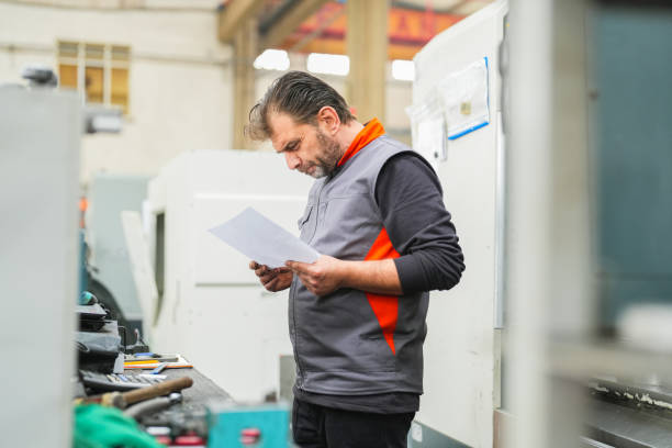 istock Male technician looking at technical drawing in front of cnc machine in industry 1923066749