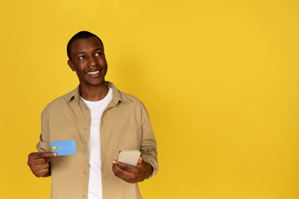 istock Smiling pensive millennial black guy use phone and credit card, dream, think 1923068923