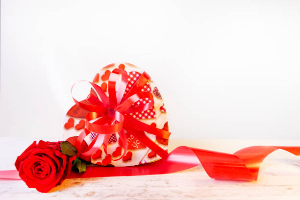 Heart shaped box, stabilized rose and red ribbon isolated on a white background. Preserved flower and a festive souvenir box as a gift for Valentine's Day. Postcard template for congratulations.