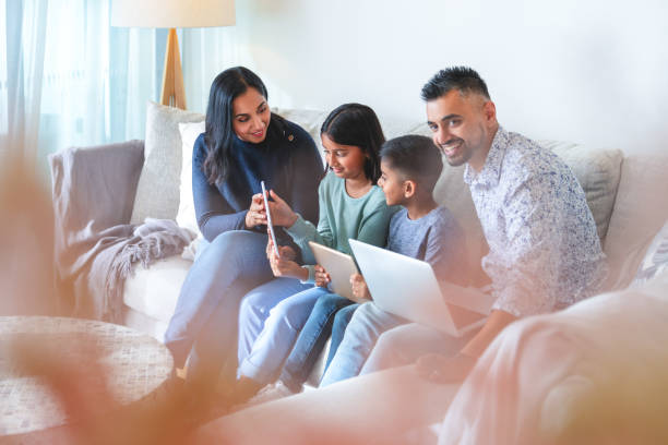 happy family with mother father and 2 children using a laptop and digital tablet on the sofa at home - father digital tablet asian ethnicity daughter imagens e fotografias de stock