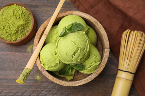 Tasty matcha ice cream, bamboo spoon with powder and whisk on wooden table, flat lay