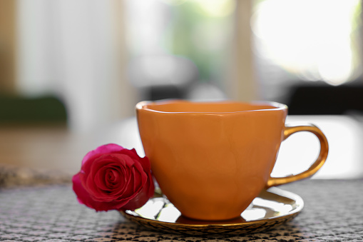 Cup of hot drink and red rose on table indoors, closeup