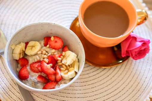 Delicious oatmeal with banana, strawberries, nuts and cup of hot drink on table, above view