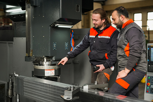 Two male technicians talking about the work on the CNC machine producing in the industry