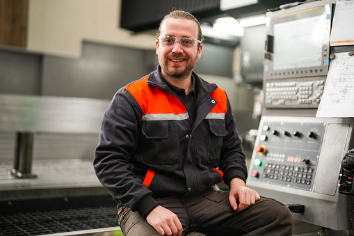 Portrait of young technician standing in front of cnc machine in industry.