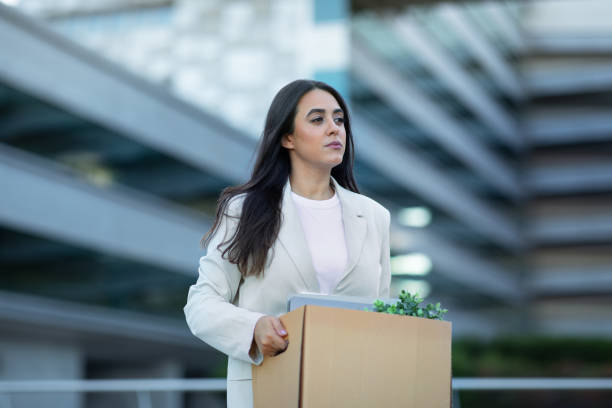 Sad business lady carrying box belongings leaving office after layoff Sad Hispanic business lady carrying cardboard box with her belongings, leaving office building after layoff, reflecting economic challenges of corporate dismissal and unemployment resignation stock pictures, royalty-free photos & images