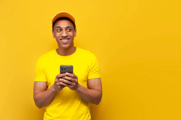 istock young african american delivery man in yellow uniform using smartphone and looking at copy space 1923141829