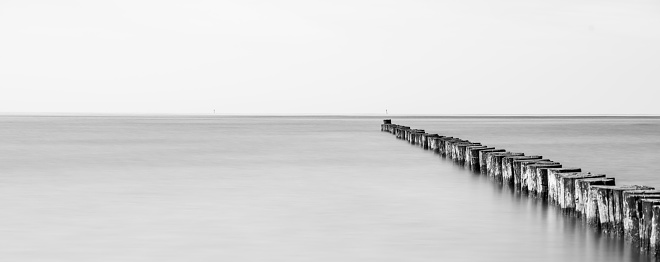 An aged wooden pier jutting out into a calm body of water, with no boats in sight