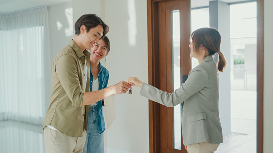 Young Asian woman real estate broker giving house keys to client after signing agreement contract. Buying a new house concept.