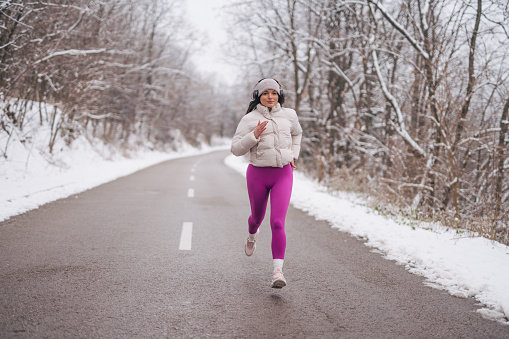 Young fitness girl running in winter sports outdoors in nature and listening to music