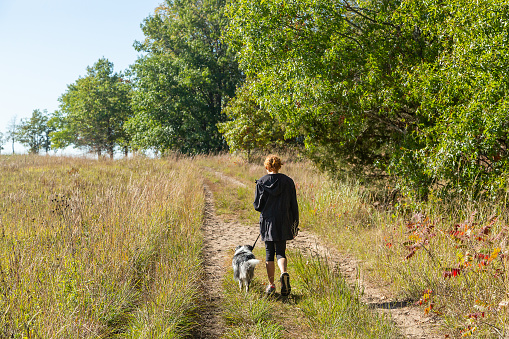 Rear view of a girl taking her Australian Shepherd dog for a walk outside on a beautiful autumn day. Taken at Crow-Hassan Park Reserve in Minnesota, USA.