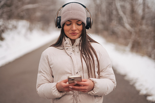 Beautiful girl holding smartphone outdoors while listen to music