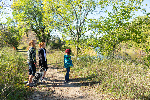 A woman and her daughter hike together on a warm fall day.  They are both dressed comfortably, have backpacks on and hiking poles in hand as they navigate the trails together.