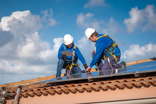 kneeling professional man and woman checking  the solar panels installation at the top of a house roof in a sunny day