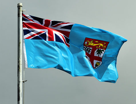 Suva, Rewa Province, Central Division, Viti Levu island, Fiji: Flag of Fiji in the wind - Blue Ensign with the shield from the national coat of arms, consisting of a shield divided quarterly by Cross of St. George and charged with a gold lion holding a cacao pod at the top. The quadrants contain sugarcane, coconut palm, bananas and a peace dove.