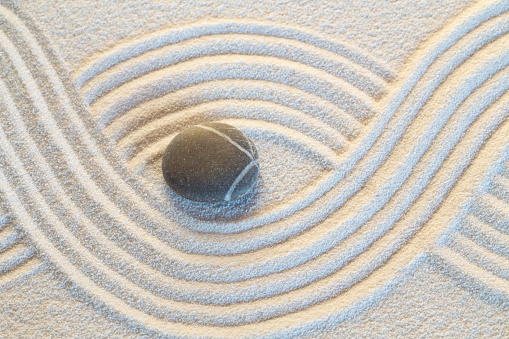 Single zen stone on white sand pattern
