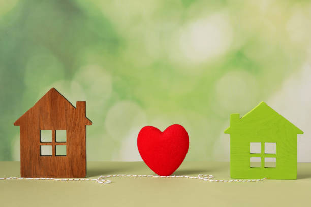 istock Red heart and decorative cord between two house models on light green background symbolizing connection in long-distance relationship 1923286340