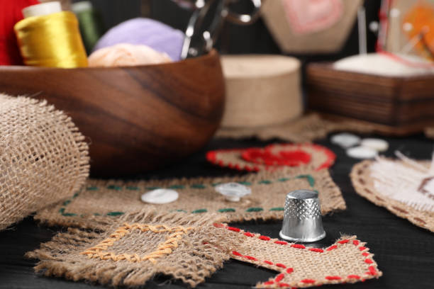 istock Pieces of burlap fabric with different stitches and thimble on black table, closeup 1923286344