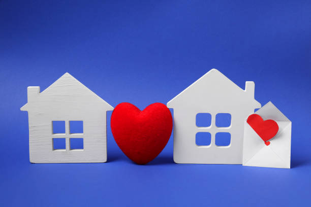 istock Long-distance relationship concept. Decorative heart between two white house models and love letter on blue background 1923286404