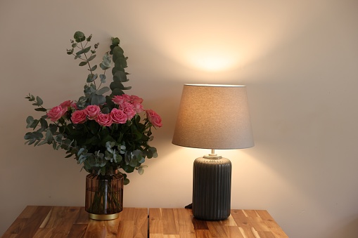 Beautiful bouquet of roses and eucalyptus branches in vase near lamp on wooden table indoors