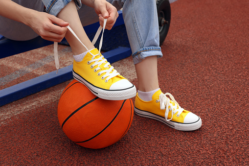Woman tying shoelace of yellow classic old school sneaker on basketball ball at outdoor court, closeup