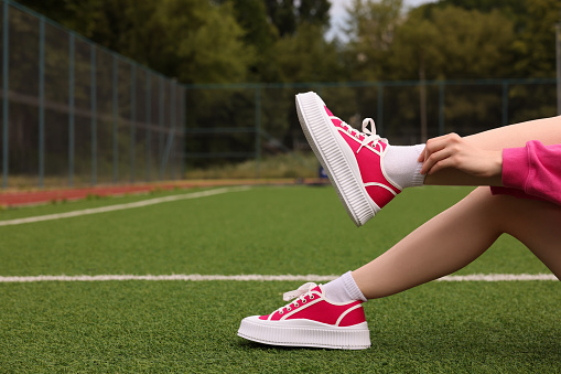 Woman wearing classic old school sneakers on green court outdoors, closeup. Space for text