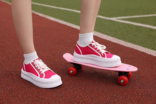 Woman with penny board wearing classic old school sneakers on sport court outdoors, closeup