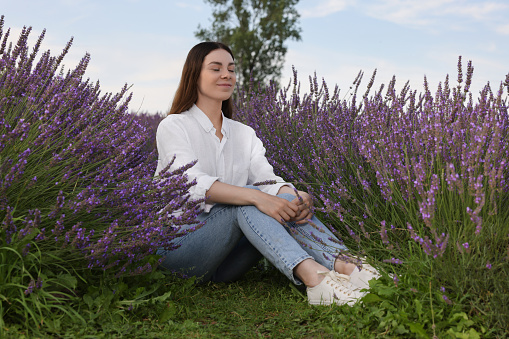 Beautiful woman sitting among lavender plants outdoors