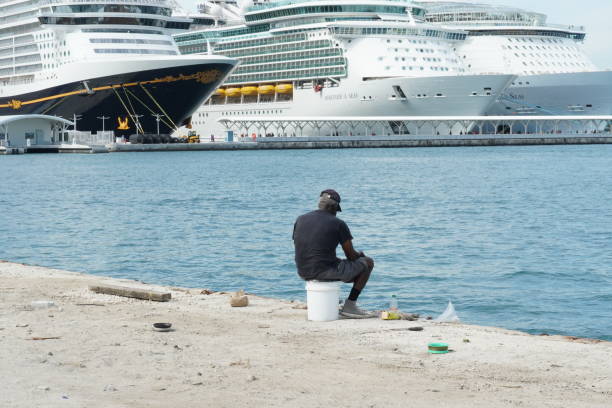 vieux pêcheur noir assis sur un seau en plastique et attrapant un poisson dans le port de nassau, aux bahamas. - leaving business landscape men photos et images de collection