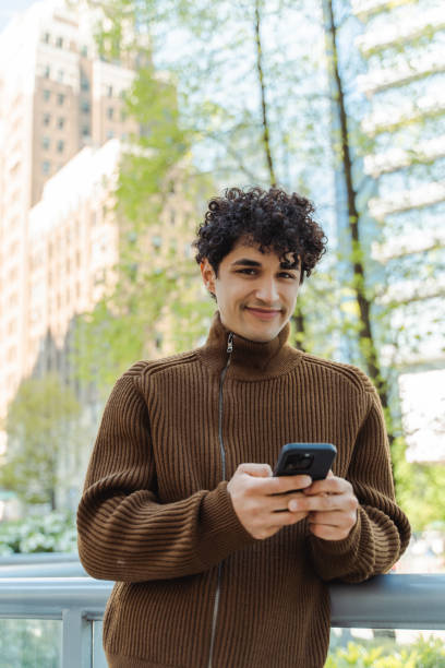 istock Vertical view of successful hispanic man holding mobile phone chatting 1923379842