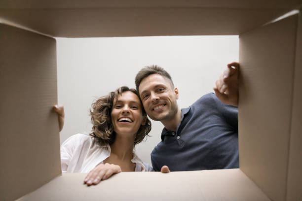 istock Cheerful young couple opening parcel, looking inside cardboard moving box 1923395973