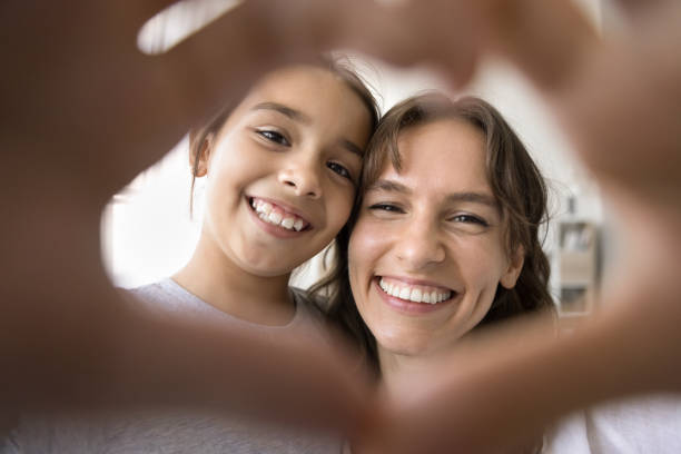 istock Cheerful kid and mom looking at camera through hand heart 1923419784