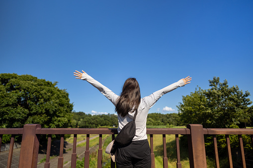 Female hiker raising hands and deep breathing on bridge in public park