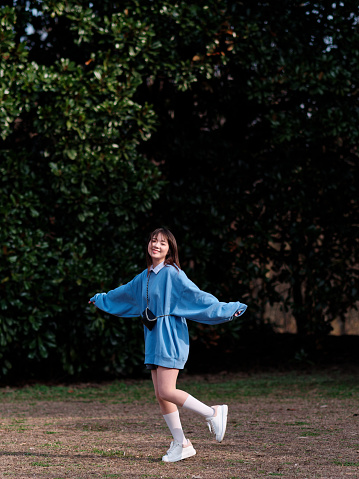 Beautiful young Chinese woman posing in sunny summer forest, wearing blue loose oversized top and miniskirt with small shoulder bag. Emotions, people, beauty, youth and lifestyle portrait.