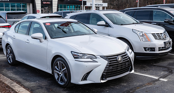 Monroeville, Pennsylvania, USA December 25, 2023 Two different used white cars, a Lexus sedan and a Cadillac SUV for sale at a dealership on a winter day