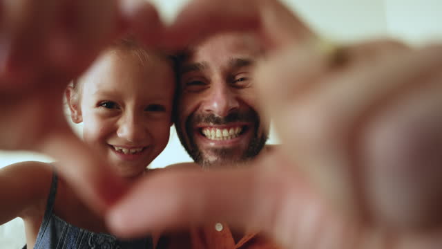 Loving dad and daughter demonstrate symbol of love to camera