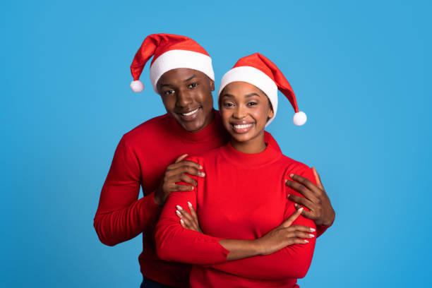 istock Happy black spouses in Santa hats embracing against blue backdrop 1923532422