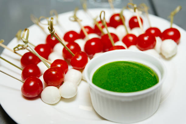 Cherry tomato and mozzarella cheese skewers accompanied by a vibrant green pesto sauce, perfect for an appetizer or party snack.