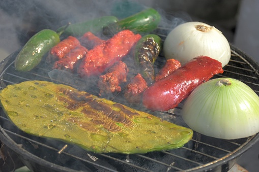 Traditional carne asada for tacos, grilled fajita beef meat with onion, nopal, jalapeno, chorizo, red sausage, and spices over coal grill and smoke