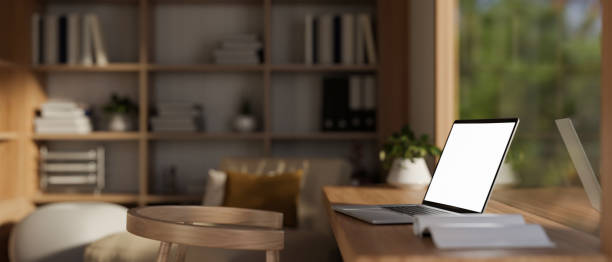 istock Side view image of a white-screen laptop computer on a wooden desk in a modern, Scandinavian room. 1923633608