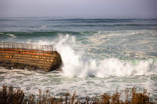 Powerful waves wash over an old pier in the water on the Pacific coast near San Diego in La Jolla