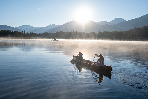 Rear view of men paddling canoe and kayak at sunset lake.