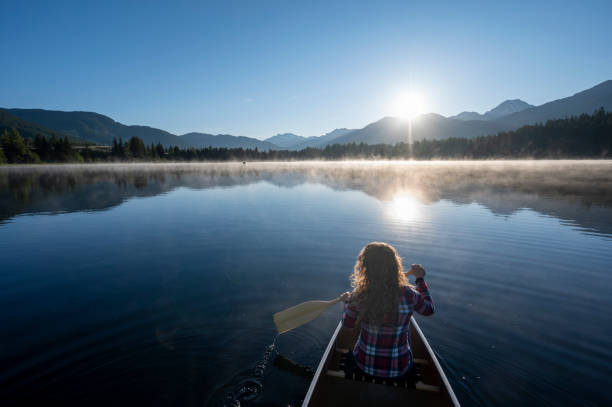 istock Girl paddles canoe on tranquil lake 1923684311
